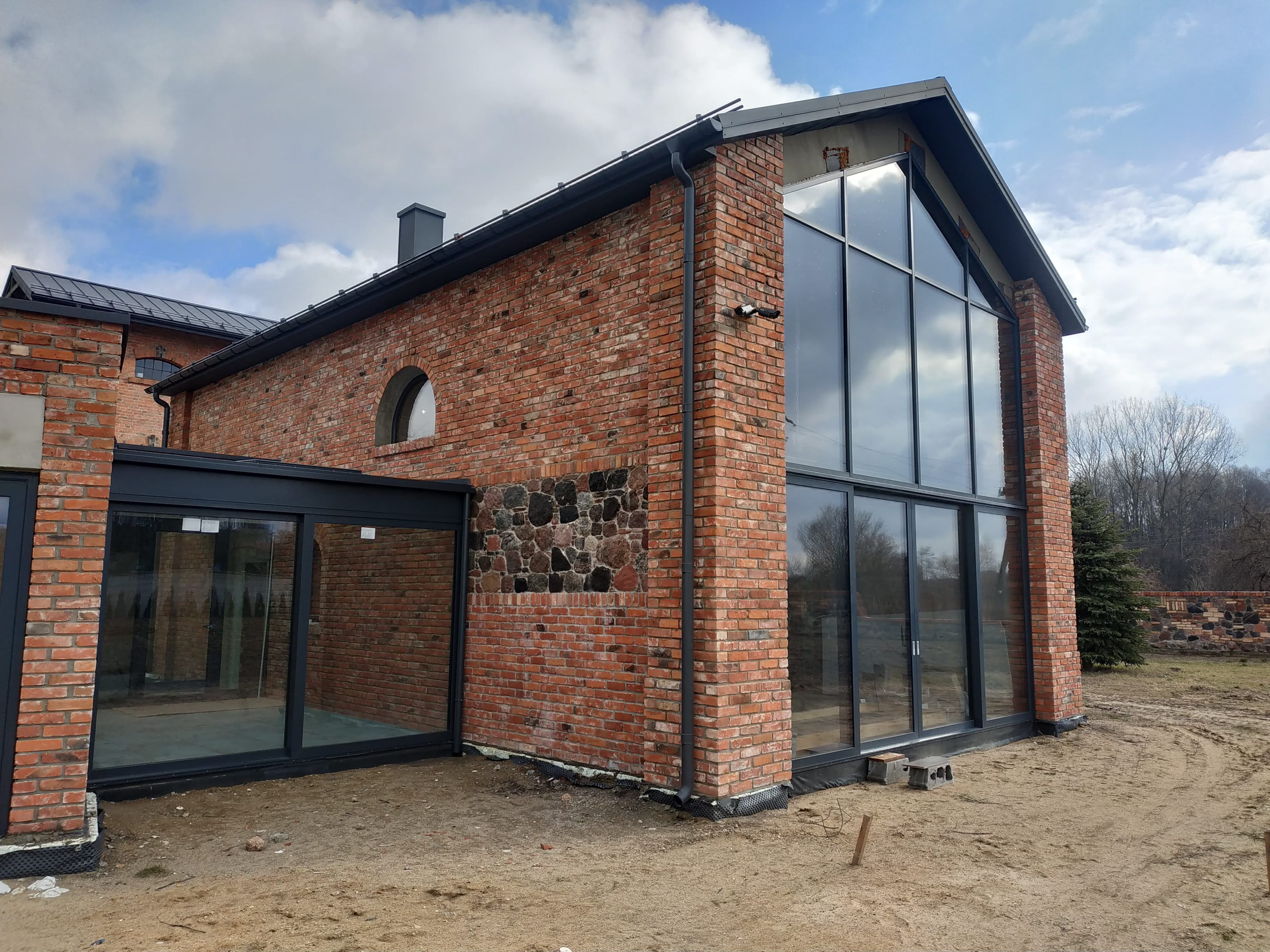 Aluminiowa fasada dwukondygnacyjna, drzwi przesuwne, drzwi wejściowe i aluminiowy przedsionek ze szklanym dachem.