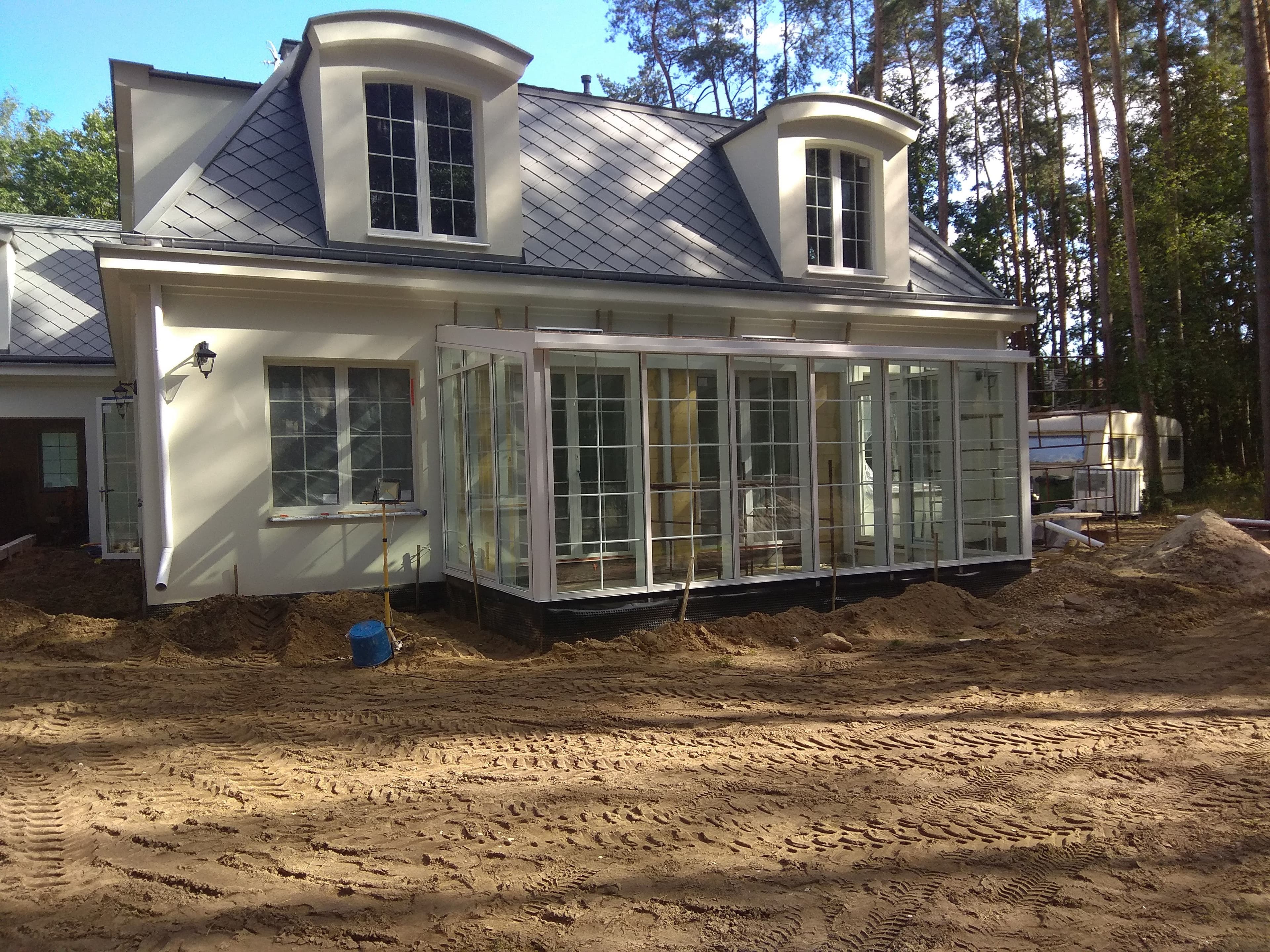 Ogród zimowy ze szklanym dachem na konstrukcji aluminiowej, białe okna aluminiowe z łukami i szprosami.