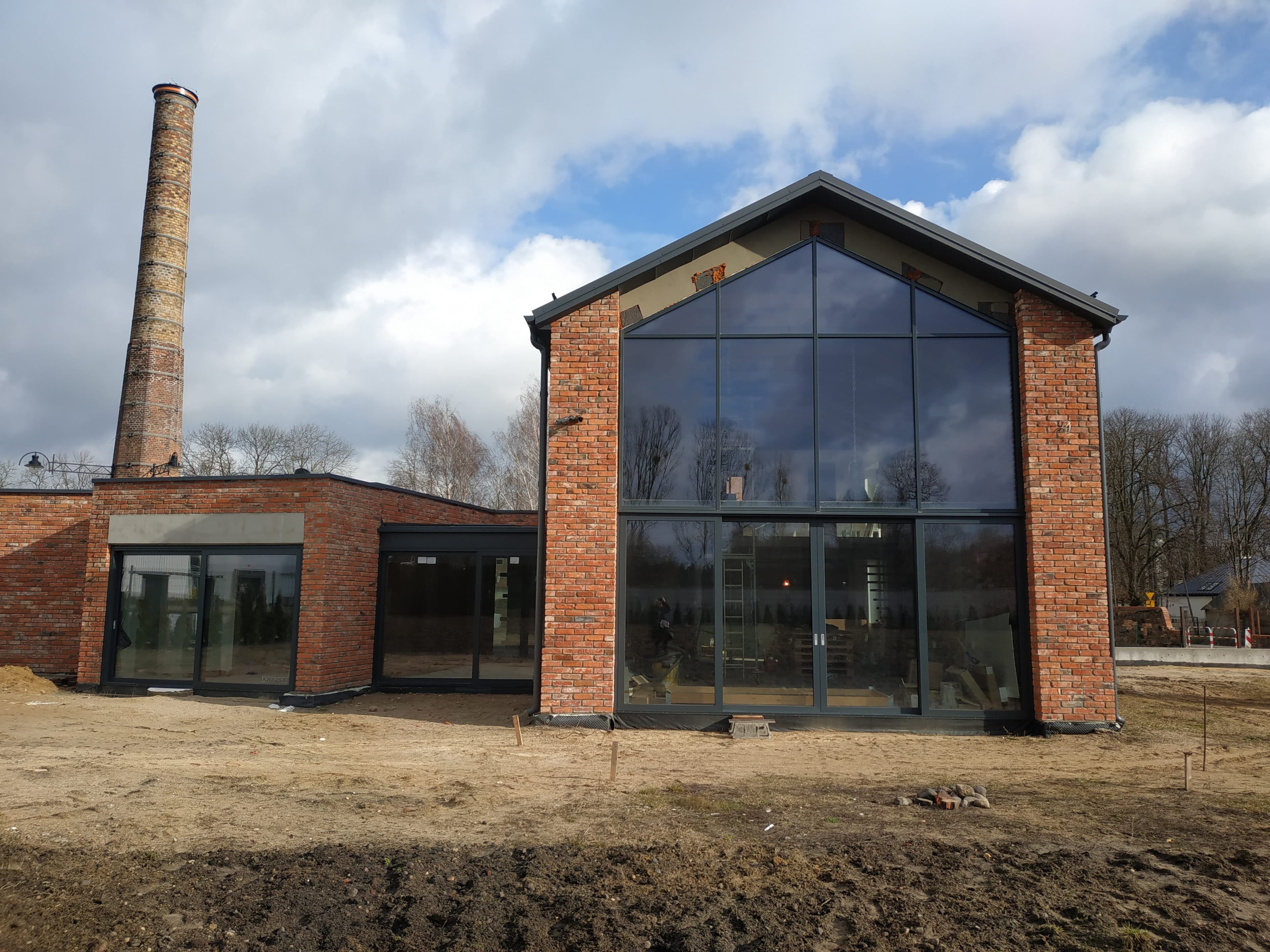 Aluminiowa fasada dwukondygnacyjna, drzwi przesuwne, drzwi wejściowe i aluminiowy przedsionek ze szklanym dachem.