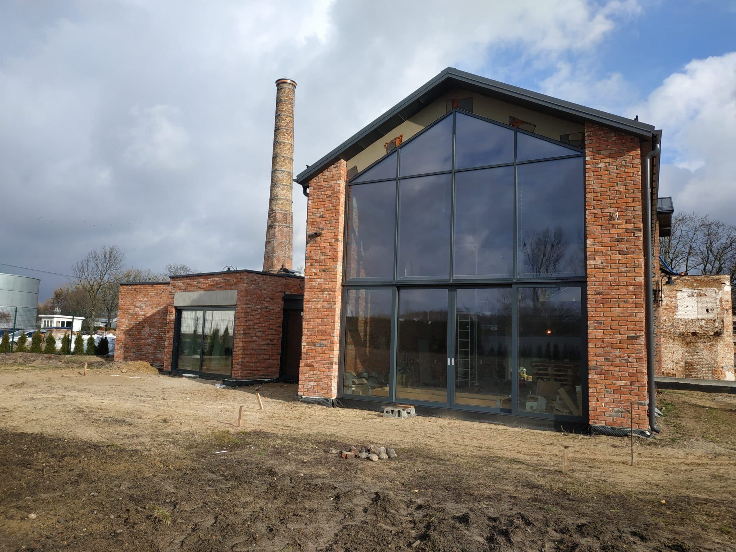 Aluminiowa fasada dwukondygnacyjna, drzwi przesuwne, drzwi wejściowe i aluminiowy przedsionek ze szklanym dachem.